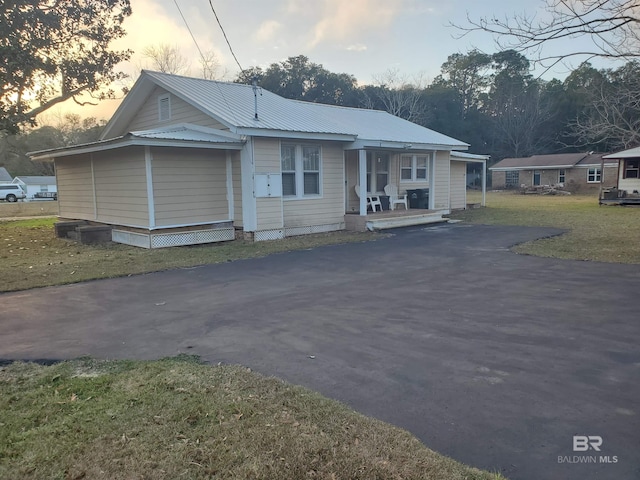 view of front of house featuring aphalt driveway, covered porch, a front yard, and metal roof