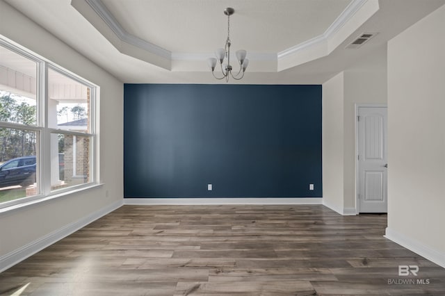 unfurnished room with visible vents, a notable chandelier, ornamental molding, wood finished floors, and a raised ceiling