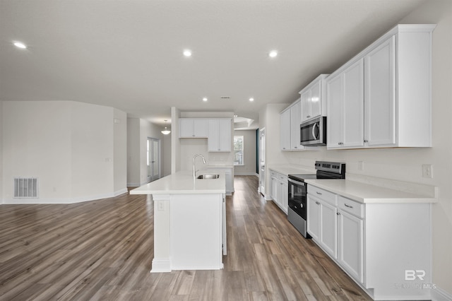kitchen with visible vents, a kitchen island with sink, a sink, wood finished floors, and stainless steel appliances