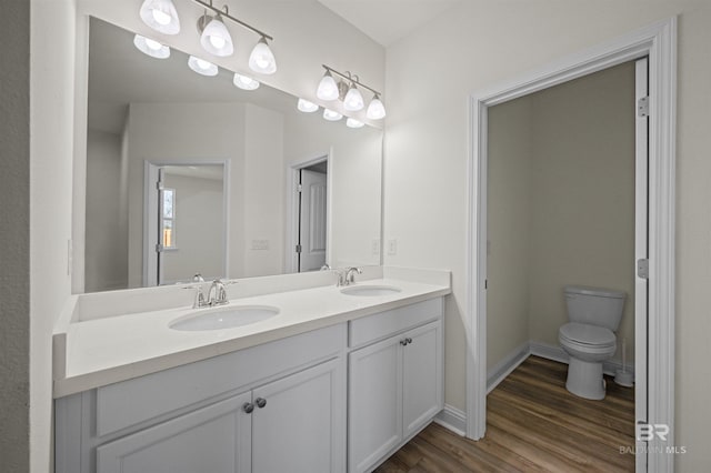 full bathroom with double vanity, toilet, wood finished floors, and a sink