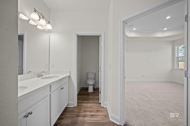 bathroom featuring baseboards, toilet, double vanity, ornamental molding, and a sink