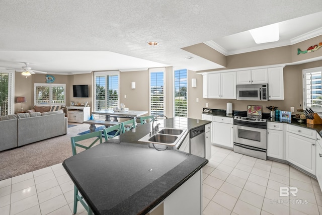 kitchen with a center island with sink, a sink, stainless steel appliances, white cabinets, and dark countertops