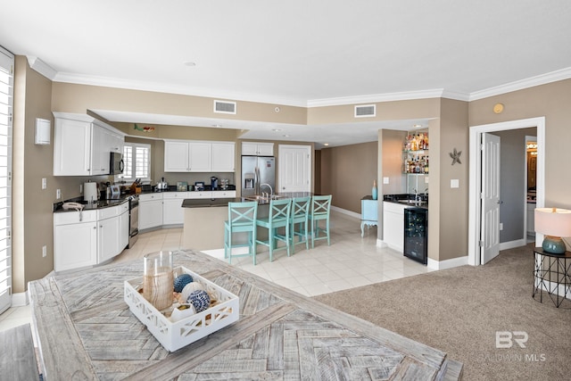 kitchen with wine cooler, white cabinets, appliances with stainless steel finishes, and an island with sink