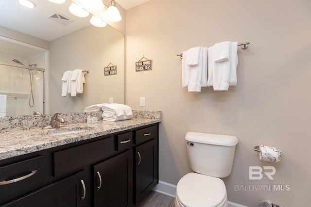 full bathroom with vanity, a shower with shower door, baseboards, visible vents, and toilet