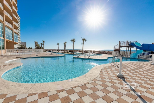 pool featuring a patio area, a jacuzzi, a water slide, and fence