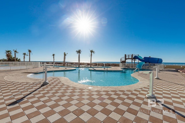 community pool with a patio area, fence, and a water slide