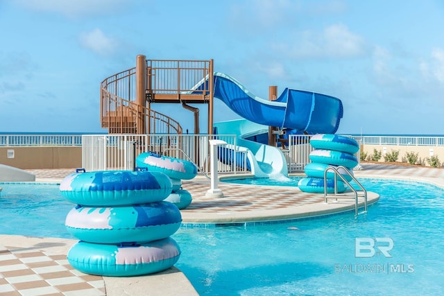 pool with a water play area, a water slide, a playground, and fence