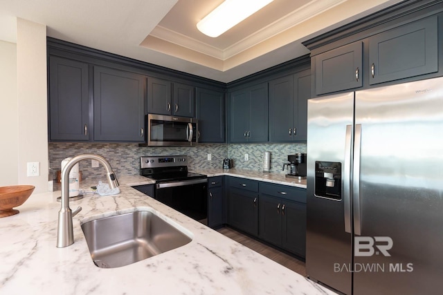 kitchen with light stone counters, a sink, crown molding, appliances with stainless steel finishes, and a raised ceiling