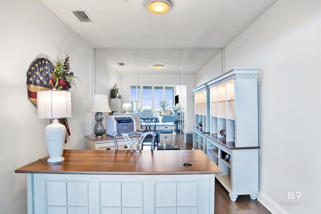 home office with dark wood-style flooring, visible vents, and baseboards