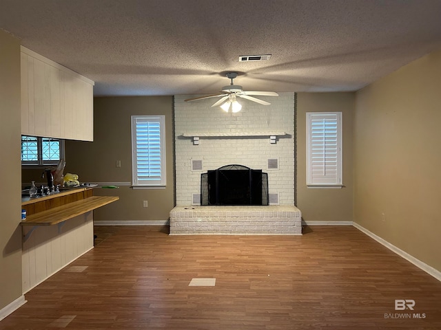 unfurnished living room featuring a textured ceiling, hardwood / wood-style floors, ceiling fan, and a brick fireplace