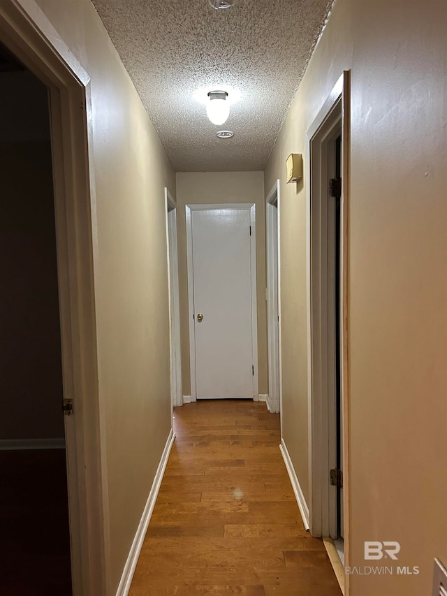 corridor with a textured ceiling and light hardwood / wood-style floors