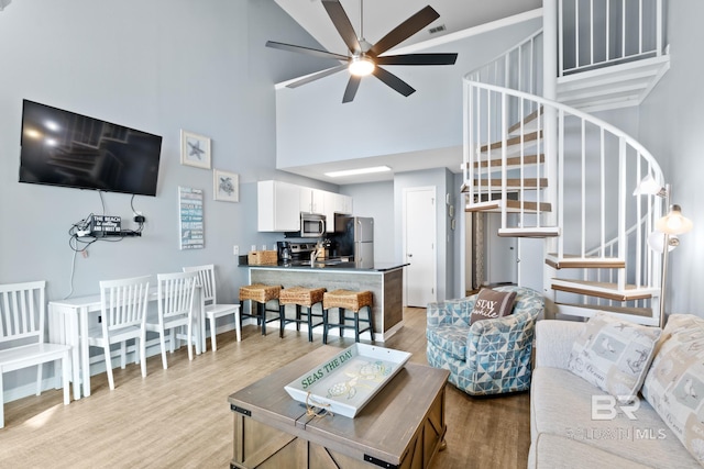 living room featuring ceiling fan, a towering ceiling, and light hardwood / wood-style floors