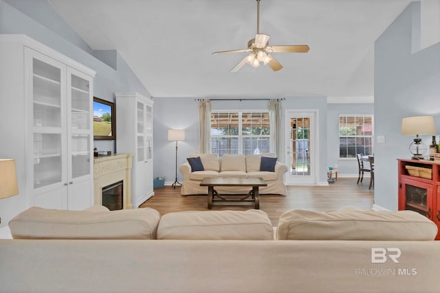 living area featuring a glass covered fireplace, wood finished floors, lofted ceiling, baseboards, and ceiling fan