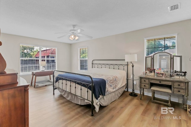 bedroom featuring baseboards, visible vents, multiple windows, and wood finished floors