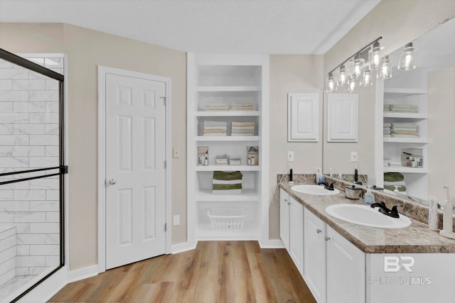 full bath featuring built in features, a shower stall, a sink, and wood finished floors