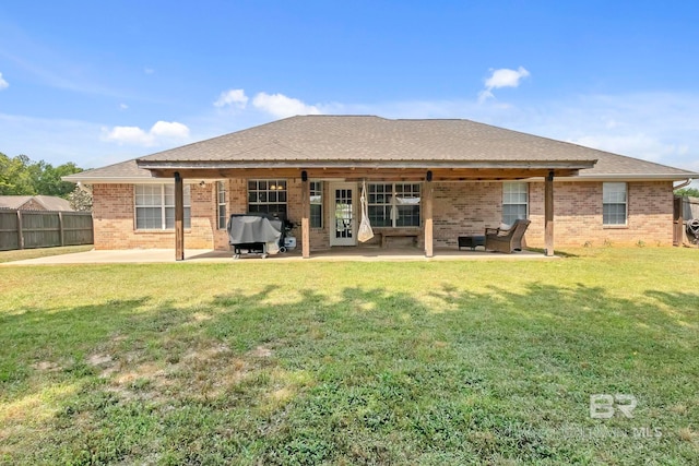 rear view of house with a patio, a lawn, fence, and brick siding