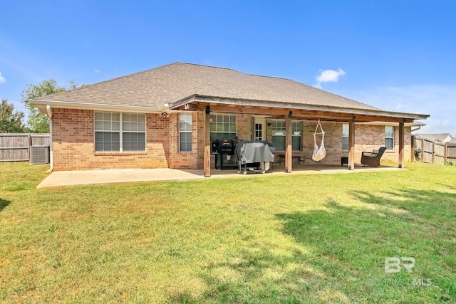 rear view of house featuring fence, a patio, brick siding, a shingled roof, and a lawn