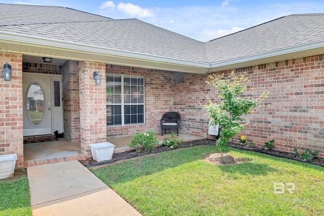 entrance to property with a shingled roof, a yard, and brick siding