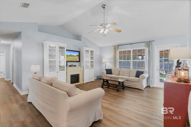 living area featuring ceiling fan, a glass covered fireplace, light wood-style flooring, baseboards, and lofted ceiling