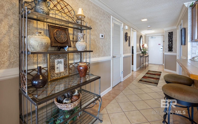 hall with light tile patterned flooring, ornamental molding, and a textured ceiling