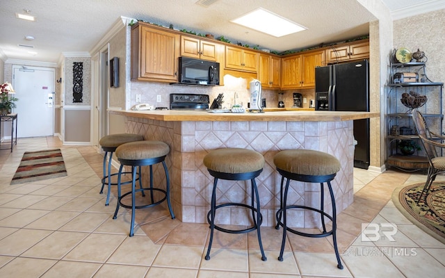 kitchen featuring light tile patterned floors, black appliances, and a kitchen bar