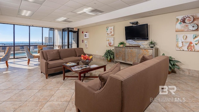 living room featuring a water view, a wall of windows, light tile patterned floors, and a drop ceiling