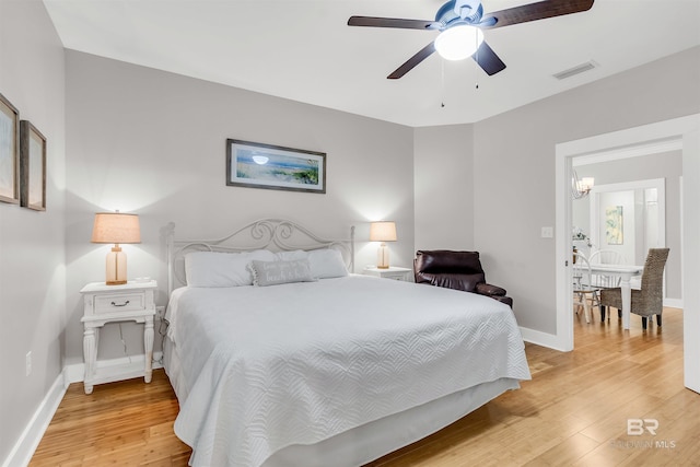 bedroom featuring baseboards, visible vents, light wood finished floors, and ceiling fan with notable chandelier