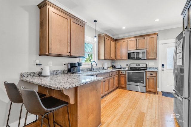 kitchen featuring appliances with stainless steel finishes, a sink, light stone counters, a peninsula, and light wood-style flooring