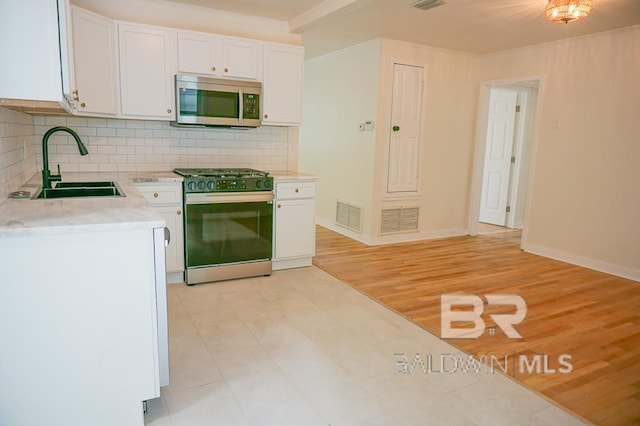 kitchen with white cabinetry, range, sink, and tasteful backsplash