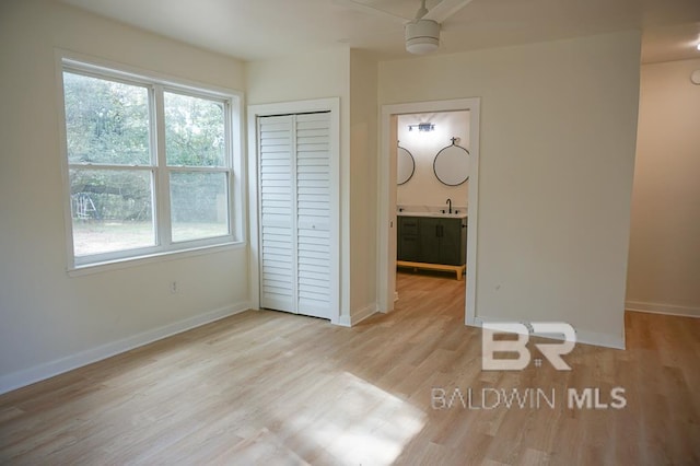 unfurnished bedroom featuring light wood-type flooring, ensuite bath, ceiling fan, sink, and a closet