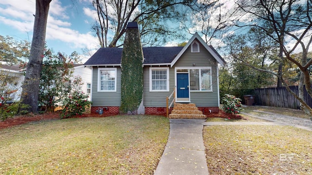 bungalow with entry steps, a front lawn, fence, and a shingled roof