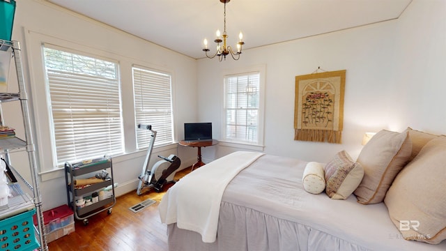 bedroom with baseboards, wood finished floors, visible vents, and a chandelier