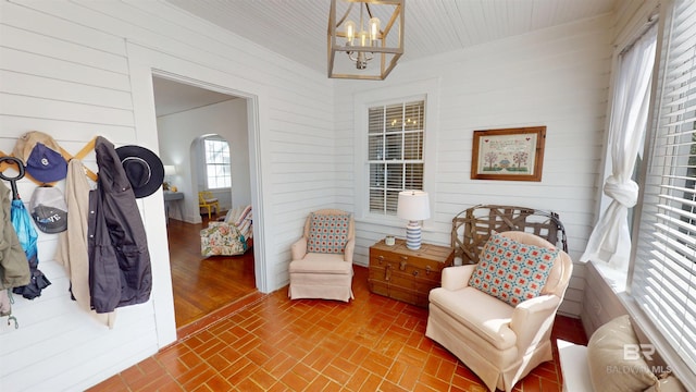 living area featuring brick floor, wooden walls, and a chandelier