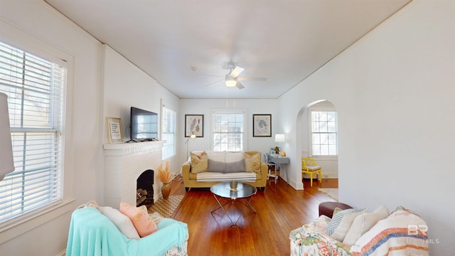 living room featuring arched walkways, a fireplace, a ceiling fan, and wood finished floors