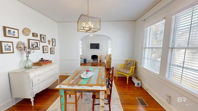 dining room featuring visible vents, wood finished floors, arched walkways, a fireplace, and baseboards