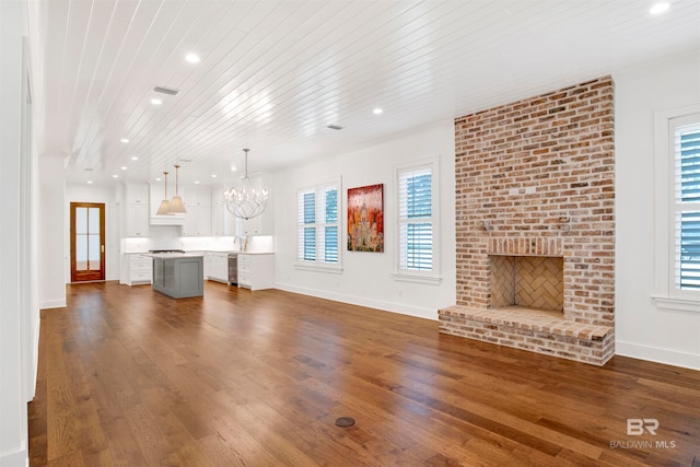 unfurnished living room featuring a brick fireplace, dark wood-type flooring, and a chandelier