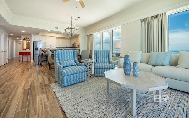 living room featuring ceiling fan with notable chandelier, light wood-type flooring, and crown molding