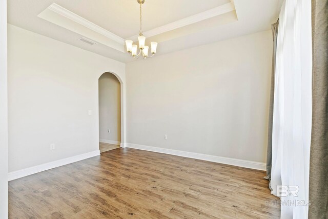 empty room with crown molding, an inviting chandelier, dark hardwood / wood-style floors, and a tray ceiling