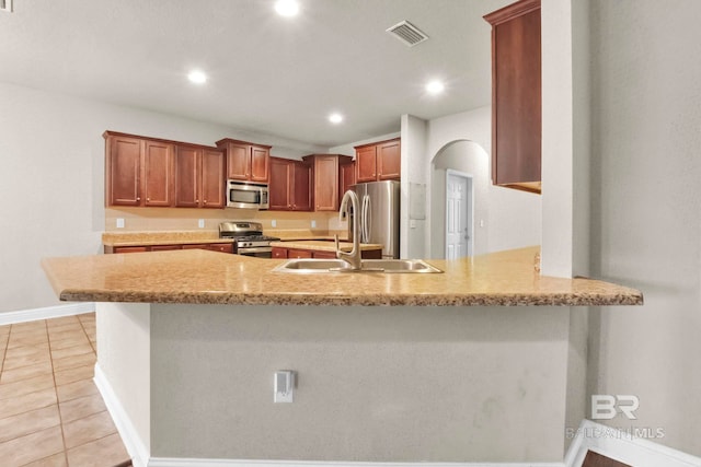 kitchen with light tile patterned floors, stainless steel appliances, light stone counters, kitchen peninsula, and sink