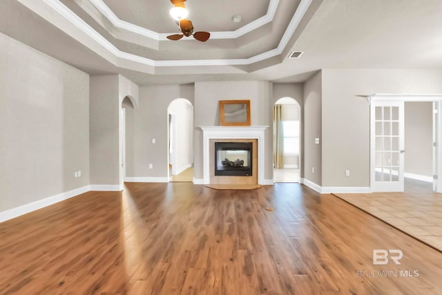 unfurnished living room with hardwood / wood-style floors, a tray ceiling, a multi sided fireplace, and crown molding