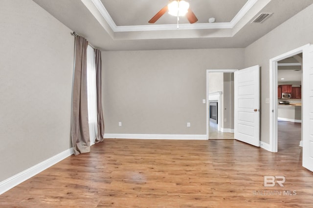 empty room with a tray ceiling, ceiling fan, wood-type flooring, and ornamental molding