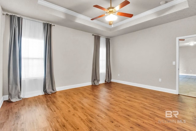 empty room with ceiling fan, a raised ceiling, wood-type flooring, and a healthy amount of sunlight