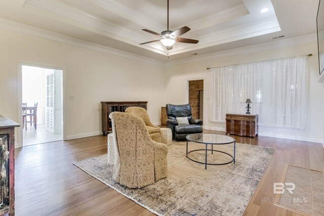 living room featuring a tray ceiling, ornamental molding, hardwood / wood-style flooring, and ceiling fan