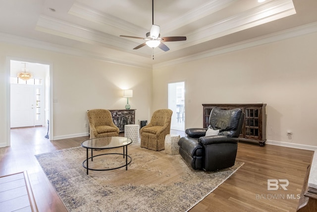 living area with a raised ceiling, wood-type flooring, and ornamental molding