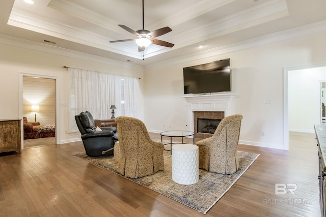 living room featuring light wood-type flooring, a tile fireplace, crown molding, and a raised ceiling