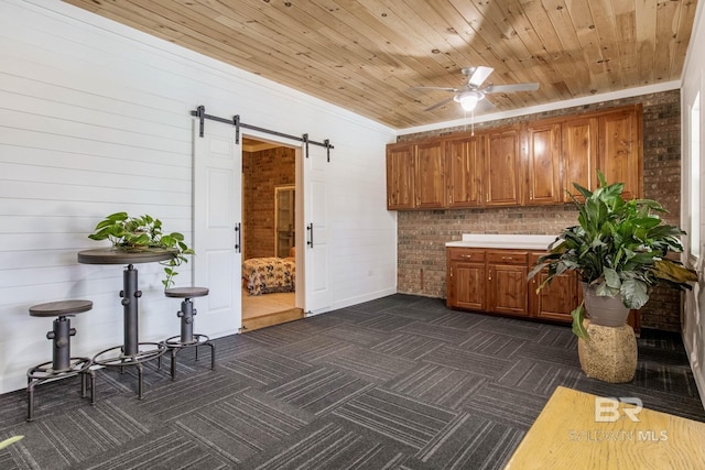 kitchen featuring dark carpet, wooden ceiling, brick wall, and a barn door