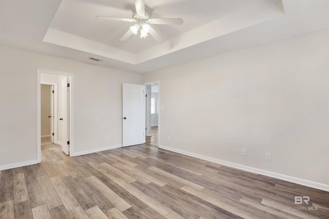 unfurnished room featuring light hardwood / wood-style floors, a raised ceiling, and ceiling fan