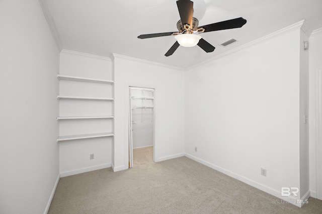 unfurnished bedroom with a closet, crown molding, ceiling fan, a walk in closet, and light colored carpet