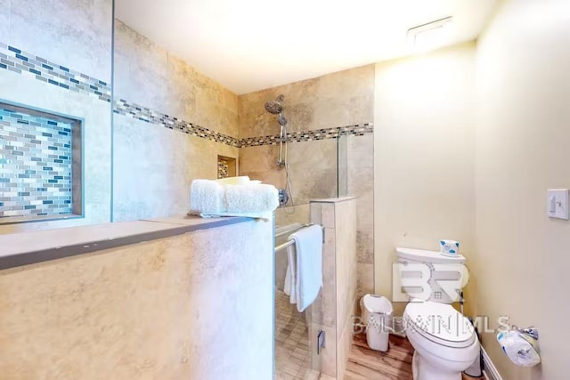 bathroom featuring hardwood / wood-style flooring, a tile shower, and toilet