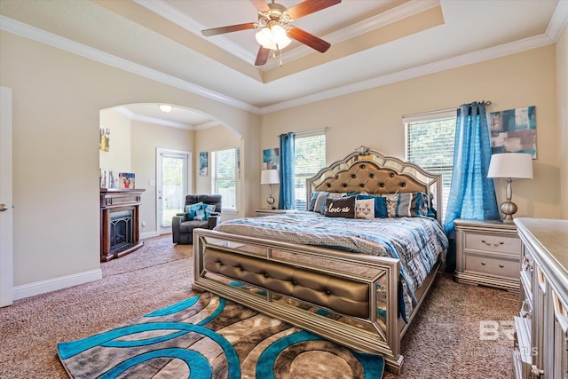 carpeted bedroom featuring multiple windows, a tray ceiling, ornamental molding, and ceiling fan